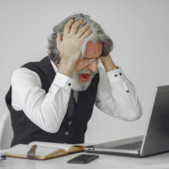 Senior businessman sitting at desk, expressing frustration with his laptop in a professional office setting.